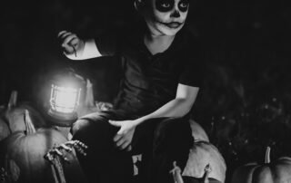 a boy in a skeleton mask sitting on a pile of pumpkins